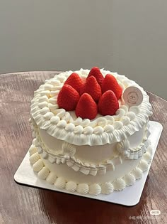 a cake with white frosting and strawberries on top sits on a wooden table