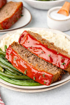 two slices of meatloaf on a plate with green beans and mashed potatoes