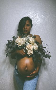 a pregnant woman with flowers on her belly is standing against a wall and posing for the camera