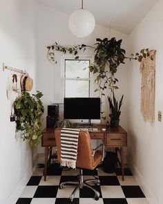 a room with a desk, computer and plants in it