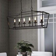 a chandelier hanging over a dining room table with white chairs and a potted plant