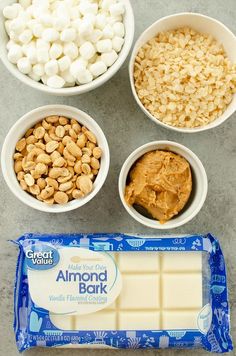 the ingredients to make almond bark are in small white bowls, including marshmallows and peanuts