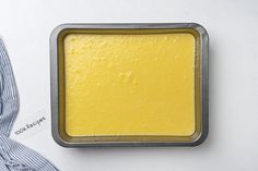 a pan filled with yellow cake batter on top of a white table next to a blue and white striped napkin