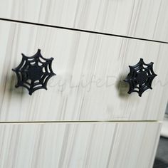 two black spider web knobs on a white cabinet