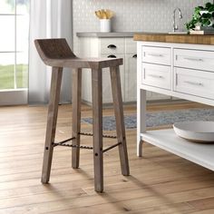 a wooden stool in a kitchen next to a white counter top and cabinet with drawers