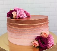 there is a pink and gold cake with flowers on the top, sitting on a plate