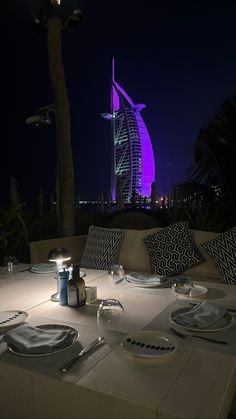 the table is set with plates, silverware and wine glasses in front of an illuminated burj