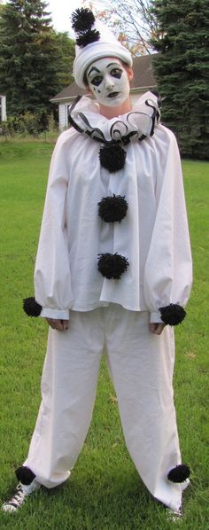 a man in a white and black clown costume is standing on the grass with his hands behind his back