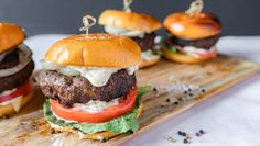 three hamburgers on a cutting board with onions and tomatoes