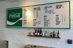 a wall mounted menu on the side of a white brick wall in a restaurant with green and white signs