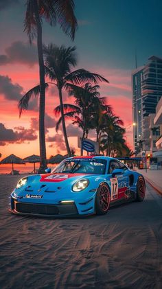 a blue sports car parked on top of a sandy beach next to palm trees at sunset