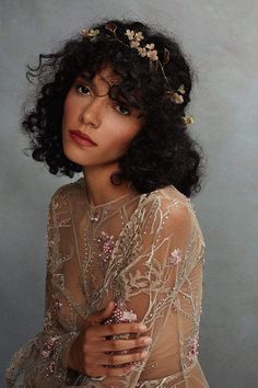 a woman with curly hair wearing a sheer top and holding her hands on her chest