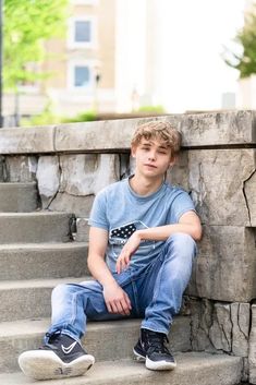 a young boy sitting on the steps in front of a building with his hand on his hip