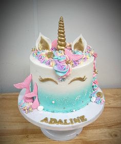 a white cake with pink, blue and gold icing has a unicorn horn on top