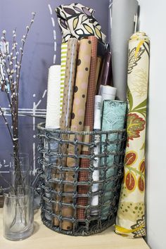 a basket filled with lots of wrapping paper next to a vase full of scissors and other crafting supplies