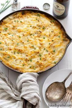 a casserole with cheese and green onions in a pan next to a bottle of beer