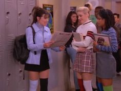 two women in school uniforms are standing next to lockers and looking at the papers