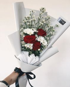 a person holding a bouquet of flowers with white and red roses in it's center