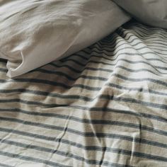 an unmade bed with white and blue striped linens on top of the sheets