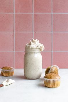 three cupcakes and a jar of frosting on a counter top with pink tiles