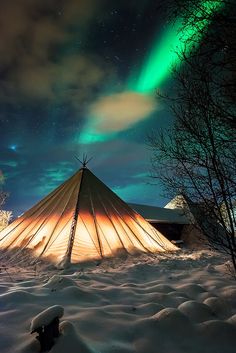 a yurt in the snow with an aurora light above it