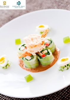 a white plate topped with cucumbers covered in sauce and garnished with scallions