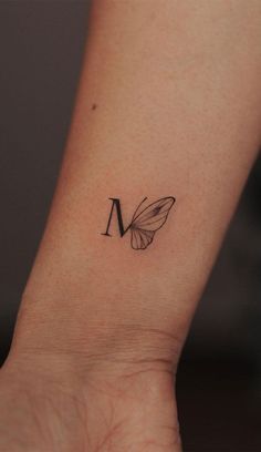 a small butterfly tattoo on the wrist that reads m and has a letter in it