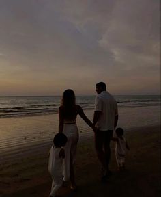 a man and woman holding hands while walking along the beach with their children at sunset