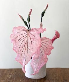 a pink flower in a white vase on a wooden table