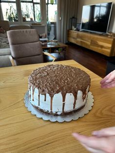 a chocolate cake sitting on top of a wooden table next to a woman's hand