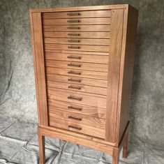 a wooden cabinet with many drawers sitting on top of a white sheeted floor next to a gray wall