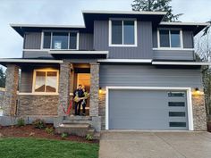 two people standing in the doorway of a house with garage doors open and lights on