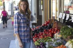 a woman standing in front of a fruit and vegetable stand