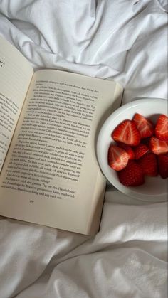 a bowl of strawberries next to an open book