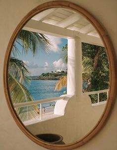 a round mirror hanging on the side of a wall next to a palm tree and ocean