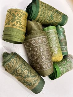 several rolls of green and gold colored material on a white tablecloth with intricate designs