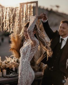 a bride and groom dancing in front of an outdoor table with lights hanging from the ceiling