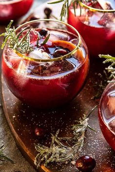 two glasses filled with red liquid and garnished with herbs on a cutting board