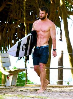 a shirtless man carrying a surfboard on the beach