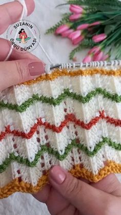 a hand holding a crocheted piece of yarn next to pink flowers and green leaves