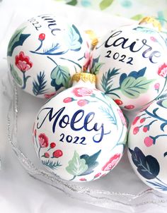 four personalized christmas ornaments are sitting on a white tablecloth with red, green and blue flowers