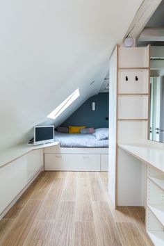 an attic bedroom with white walls and wooden floors, built in shelving units on either side of the bed