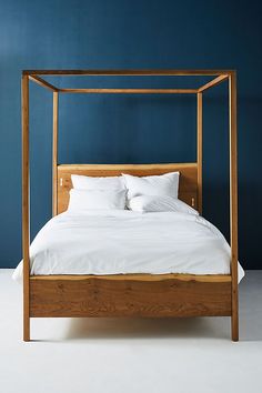 a bed with white sheets and pillows in a blue walled room that looks like it has been made into a four poster bed