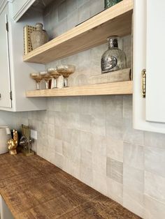 a wooden counter top in a kitchen next to white cupboards and shelves with glassware on it