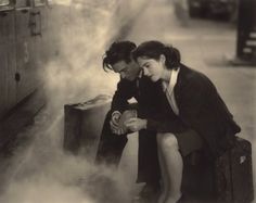 two women sitting on suitcases looking at something in the air with steam coming from them