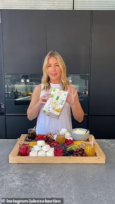 a woman standing in front of a tray full of cheese and jams, holding up a bag