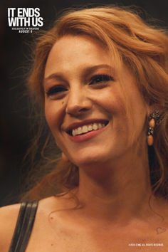 a woman with red hair smiling and wearing large gold hoop earrings on her left ear