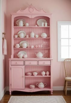 a pink china cabinet with dishes on it