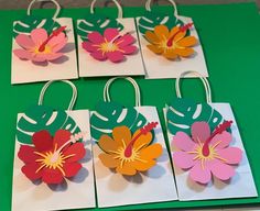 four flower shaped gift bags are on a green table with white and red tags in the shape of flowers