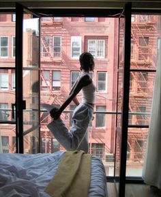 a woman standing on top of a bed in front of a window next to a building